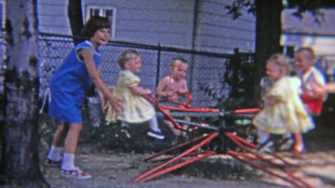 FLINT, MICHIGAN 1965: Ringleader troublemaker girl recklessly spinning small children on backyard playground toy.