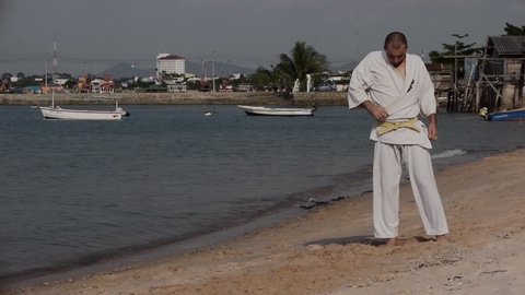Single Combat Motion Slow Karate Kimono Stock Video Footage Man on the beach practicing, he does exercise. Behind him ships, seascape, sky, summer hdv Static, Hd, Hidef, Fx, Definition, High