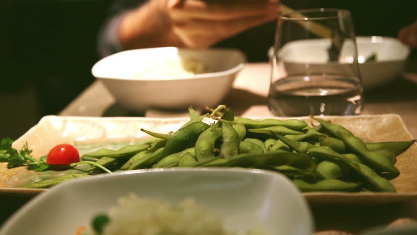 man eating eda mame, a typical japanese food, beans rich in protein and rice at sushi bar