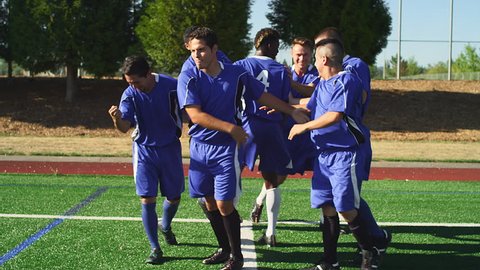 A soccer player makes a goal and the team hugs and celebrates