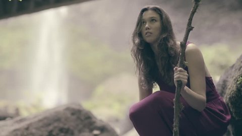Beautiful Bohemian Woman Sits Under Tree, Leaves Fall Around Her, Magical, Waterfall In Background (Slow Motion)