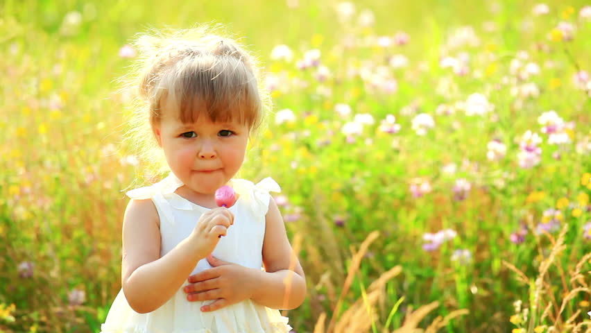 Portrait of child in the field licking lollipop