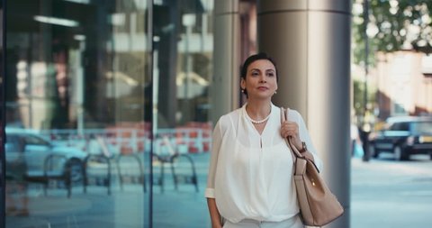 Smart Middle Eastern businesswoman using smartwatch commuting to work entering glass corporate building smiling