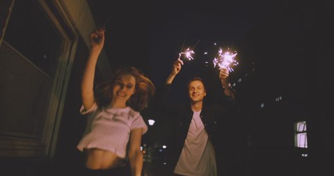 Young couple walking in Slow Motion close together on a city street at night while celebrating with sparklers - Βίντεο στοκ