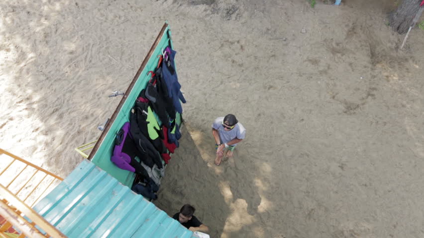 Young people on the beach taking of sports equipment storeroom. View from top.