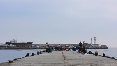 YALTA, UKRAINE, NOVEMBER 11, 2014: Fishermen fishing on the pier. Fishing is the activity of trying to catch fish. Techniques for catching fish include hand gathering, spearing, netting and trapping.