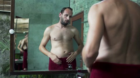 Young man in towel checking his stomach in bathroom
