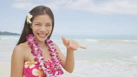 Happy woman girl standing on Hawaiian beach at Hawaii vacation. Asian Caucasian woman wearing flower lei garland and Aloha clothing showing Shaka hand sign on travel. RED EPIC SLOW MOTION.