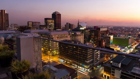Medium timelapse at nightfall showing the view from a rooftop balcony across New Town. Jeppes town and the city centre of Johannesburg during traffic with people in the streets, buildings and taxis