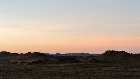 A static timelapse of vast arid landscape scene and wide open spaces with mountains and rocky hills in a semi-desert location at sunset while the night falls. 4K
