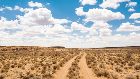 A scenic daytime drive time lapse on a gravel road with two dirt tracks in a grassy landscape setting with a blue sky and scattered clouds, front point of view. 4K