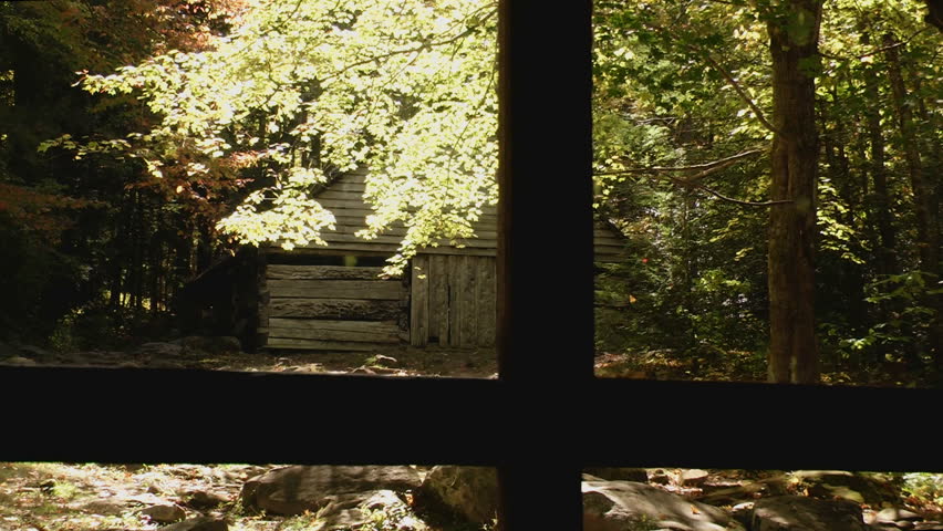 Rustic cabin in early autumn in the Great Smoky Mountains with dark shadows and some autumn color as seen from a window pane from another historical cabin