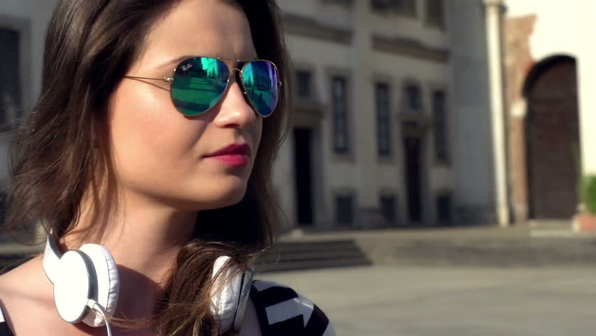Beautiful woman with colorful sunglasses standing on the square, steadycam shot
