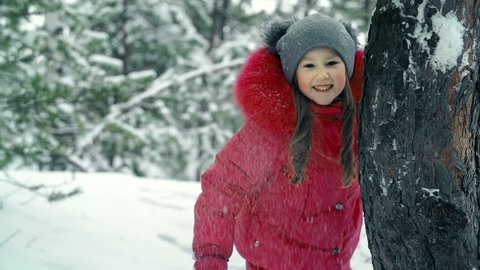 Cheerful little girl hiding behind a tree trunk during snowball fight 