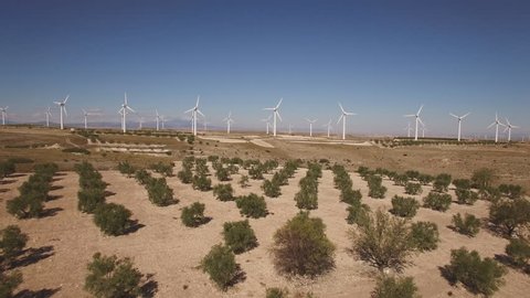Aerial view of Modern Wind turbines large array over tree field, sliding camera, approaching. 4K