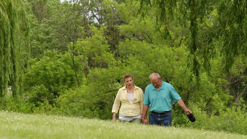 Senior couple walking dog through the park, closer shot