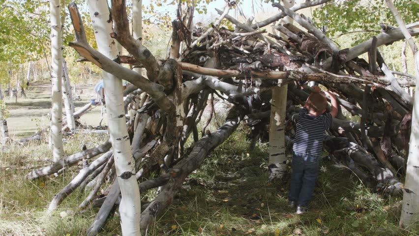 A little boy plays in a stick hut he built while camping with his family