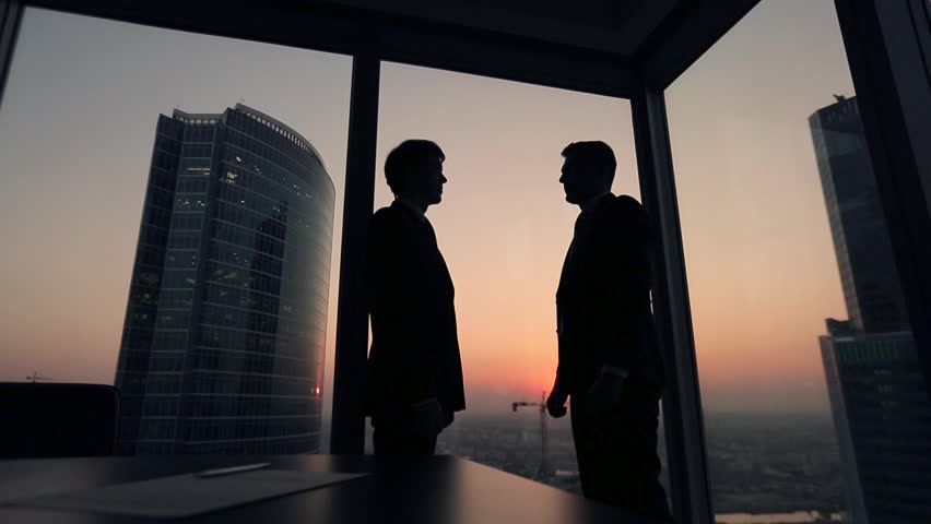 Two businessmen partners handshake in office. Silhouettes at sunset outside the window. Royalty-Free Stock Footage #12411758