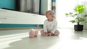 baby sitting in sunny living room on the ground and enjoy a teddy bear