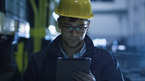 Technician in Glasses and Hard Hat Using Tablet in Industrial Environment. Shot on RED Cinema Camera in 4K (UHD).