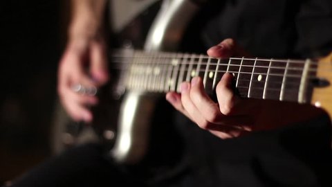 Electric guitar. Gray-black guitar. Musician plays rock music. The energetic game of rock style. Black background. Fast guitar solo. Six strings. Pluck the strings. Game mediator. Rock and roll.
