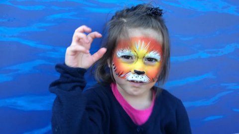 Young Jewish girl (female age 5-6) with lion face painting roaring like a lion on Purim Jewish holiday festival. party. Real people. Copy space