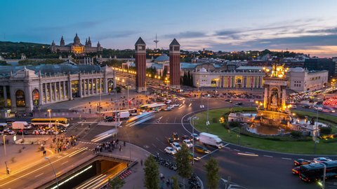Spanish Square aerial view in Barcelona, Spain at night. This is the famous place with traffic light trails, fountain and Venetian towers, and National museum at the background. Blue sky, time-lapse 