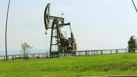Oil pump and green grass in Baku, Azerbaijan, near the Caspian Sea, with nice dark sky background and young man with bicycle crossing