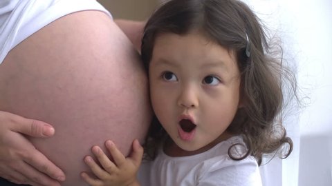 Curious little girl listening to her pregnant mother's belly,dolly shot, slow motion
