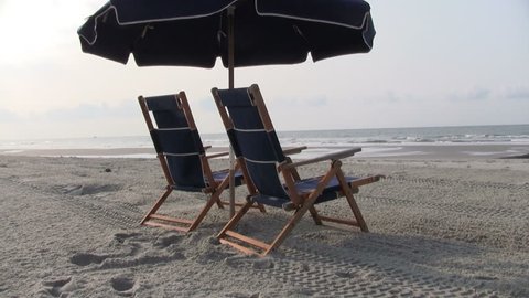 HD of two blue beach chairs with covered umbrella facing the ocean 