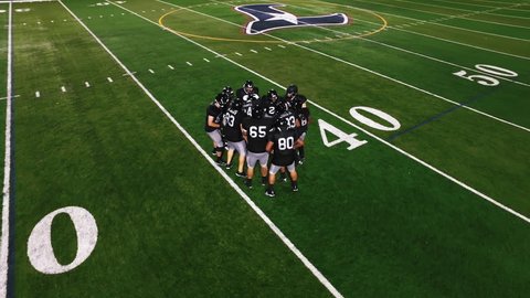 The camera spins from above as a football team in a huddle gets hyped before a game