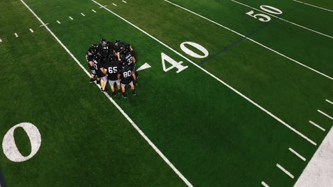 The camera spins from above as a football team in a huddle gets hyped and runs onto the field