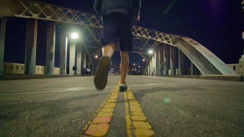 Man in dark hoodie running away in the middle of historic 6th Street Bridge viaduct in Los Angeles. Slow motion.