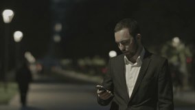 Portrait of handsome adult business man communicate by phone in good mood, while standing in the city street,business man reading messages,stylish brunette using cell phone at evening outdoors, park