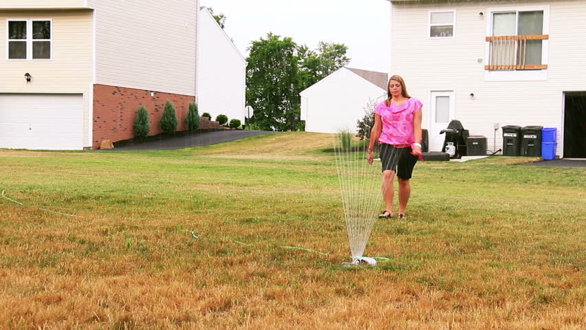 A female homeowner moves the sprinkler in her backyard.