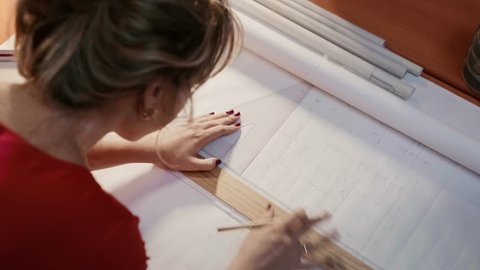 University student of Interior Design doing homework, completing housing project for final exam. The girl draws lines on a blueprint with a rule in her studio. Closeup, dolly shot