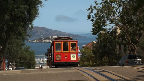 a red cable car with a distant alcatraz island in san francisco, california