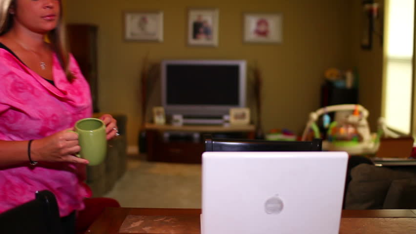 A woman sits and checks her email on her laptop computer at the kitchen table.