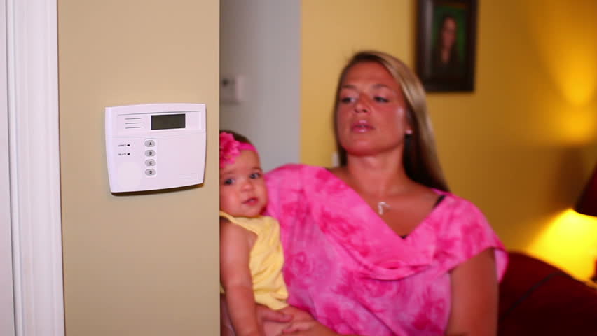 A woman with her baby confidently arms her home security system.