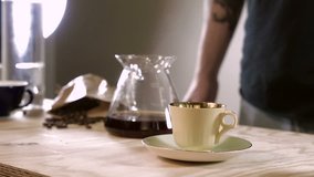 Professional barista serves hand brewed coffee into old-fashioned cup. Side view.