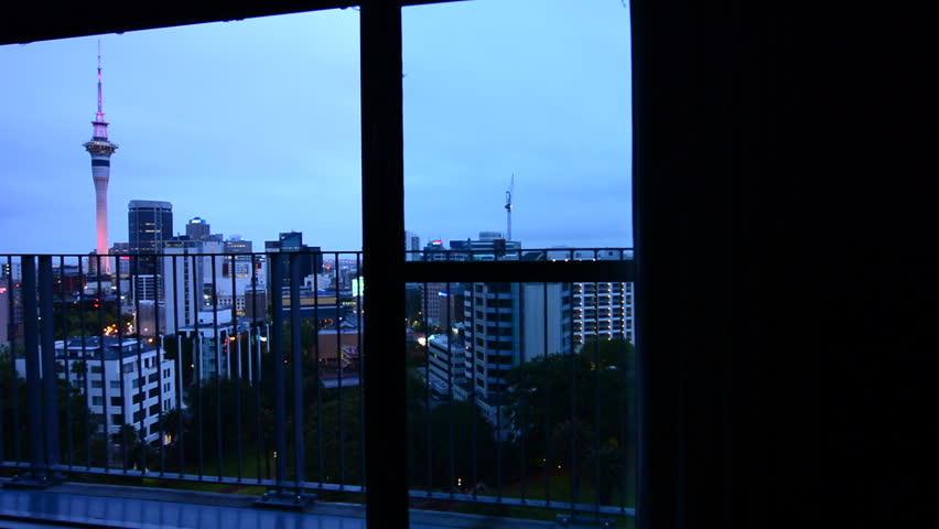Panning motion on a big widow with aerial urban view of Auckland city skyline at dusk.