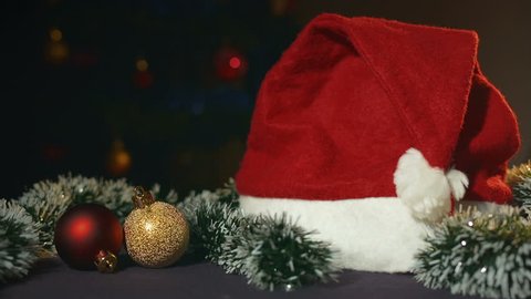 Cap of Santa Claus, red and gold Christmas balls and trumpery lying on background sparkling Christmas tree.