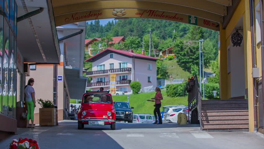 A small red yugo is arriving at a doughnut place. The day is beautiful and sunny