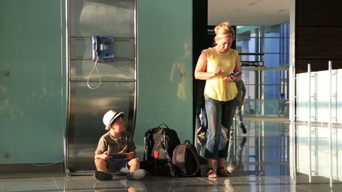 Woman using her smart phone, child using digital tablet while waiting at the airport.