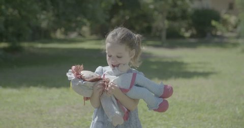 A little girl playing with a doll outdoors on a lawn