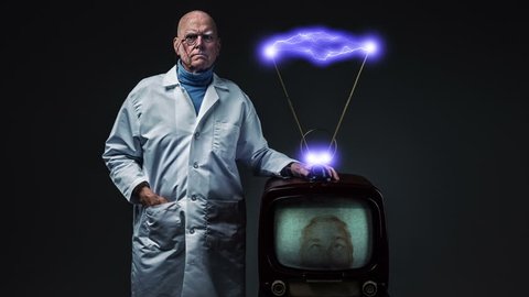 Evil genius in white lab coat standing next to vintage television with electrified rabbit ear antennae
