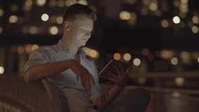 young caucasian man having a video chat conversation using a tablet computer outdoors at night. modern lifestyle communicate background