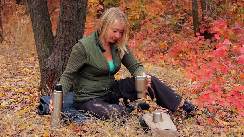 Blonde girl drinks coffee after running in the autumn forest