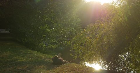 Man is Lying on The Ground at The Lake Bank, Sun Rays, Man's Silhouette, Backpack is under His Head, Man Has Stood Up, Man Shakes Off, Takes Backpack and Goes Away toward Camera, Man in Glasses, sun