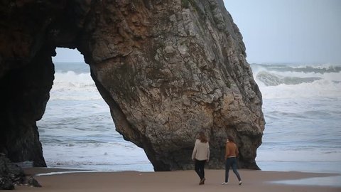 Cinemagraph Loop -Two people walking under rocks on wavy beach - motion photo Stock Video